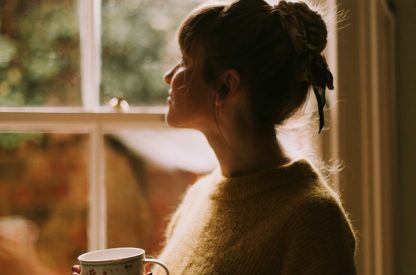 hangement d’heure : une femme tient une tasse de café près d’une fenêtre